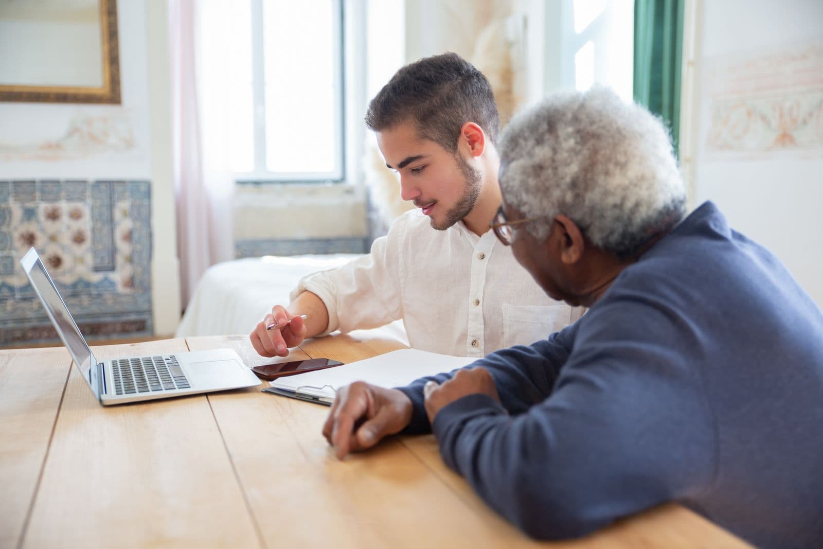 A younger man helping an older man with a laptop at a table at home