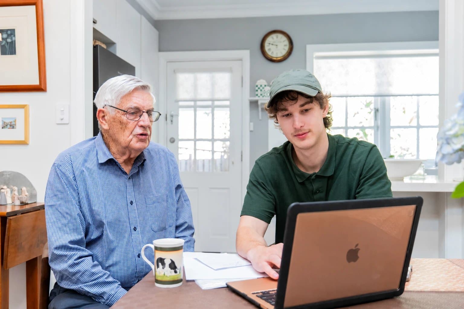 A technician helping an older man with a laptop at the kitchen table